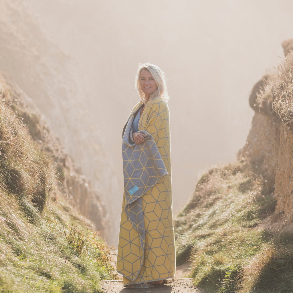 woman standing by the coast wearing a grey and yellow geometric king size blanket