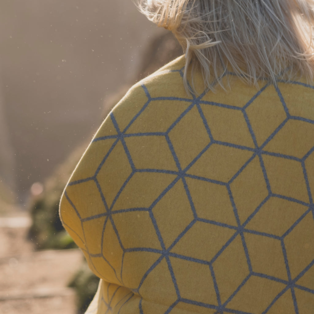a blonde woman with a yellow mustard and grey geometric blanket around her shoulders