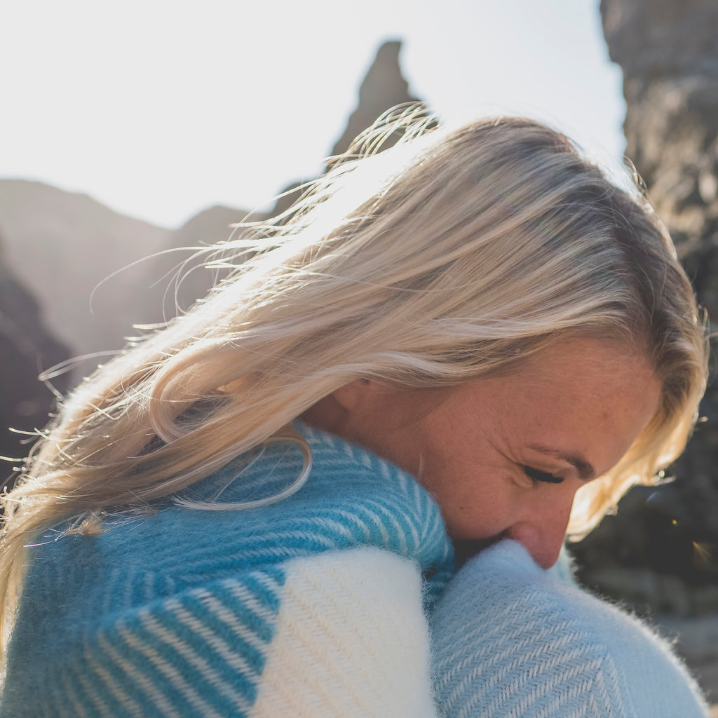 woman wrapped in blue, cream and turquoise wool blanket on beach